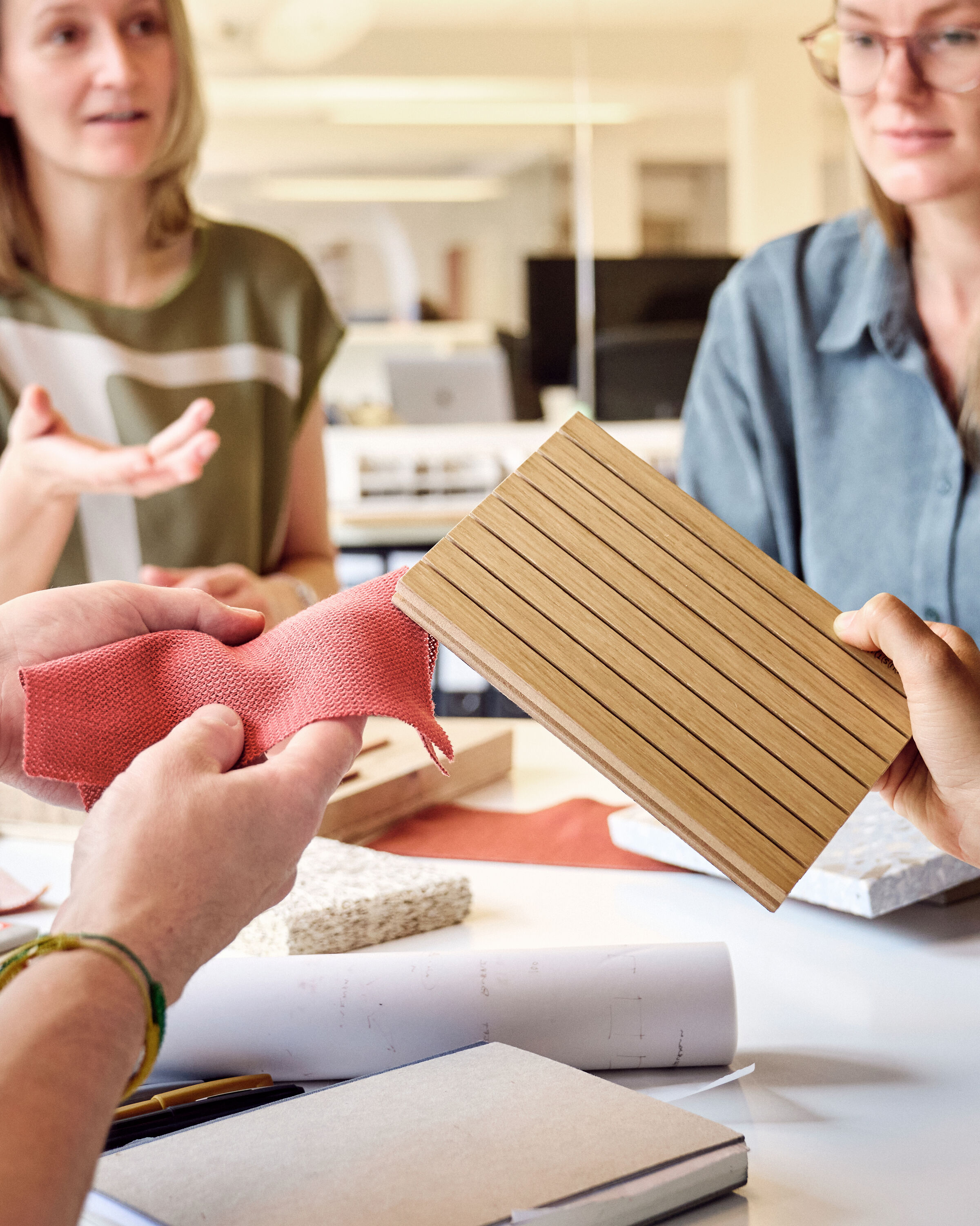 Eine Gruppe von Architekten sitzt an einem runden Tisch. Sie halten verschiedene Materialmuster in der Hand und diskutieren darüber