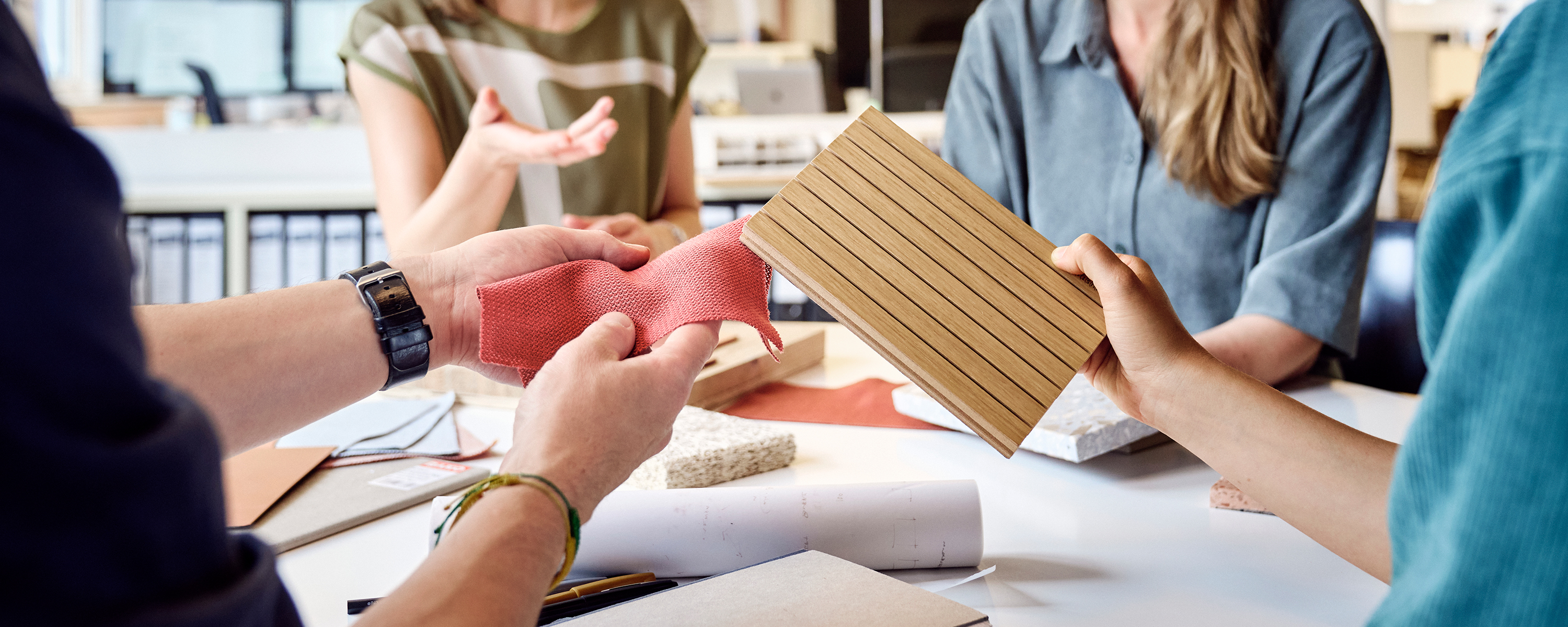 Eine Gruppe von Architekten sitzt an einem runden Tisch. Sie halten verschiedene Materialmuster in der Hand und diskutieren darüber