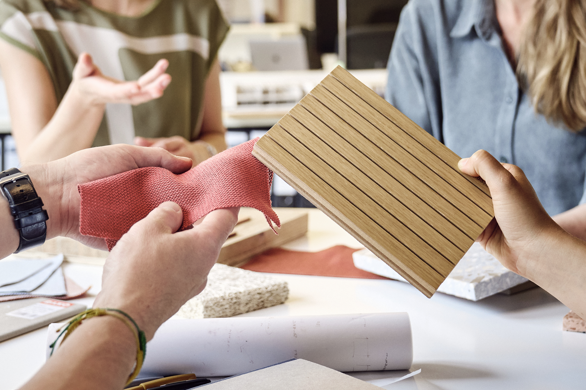 Eine Gruppe von Architekten sitzt an einem runden Tisch. Sie halten verschiedene Materialmuster in der Hand und diskutieren darüber