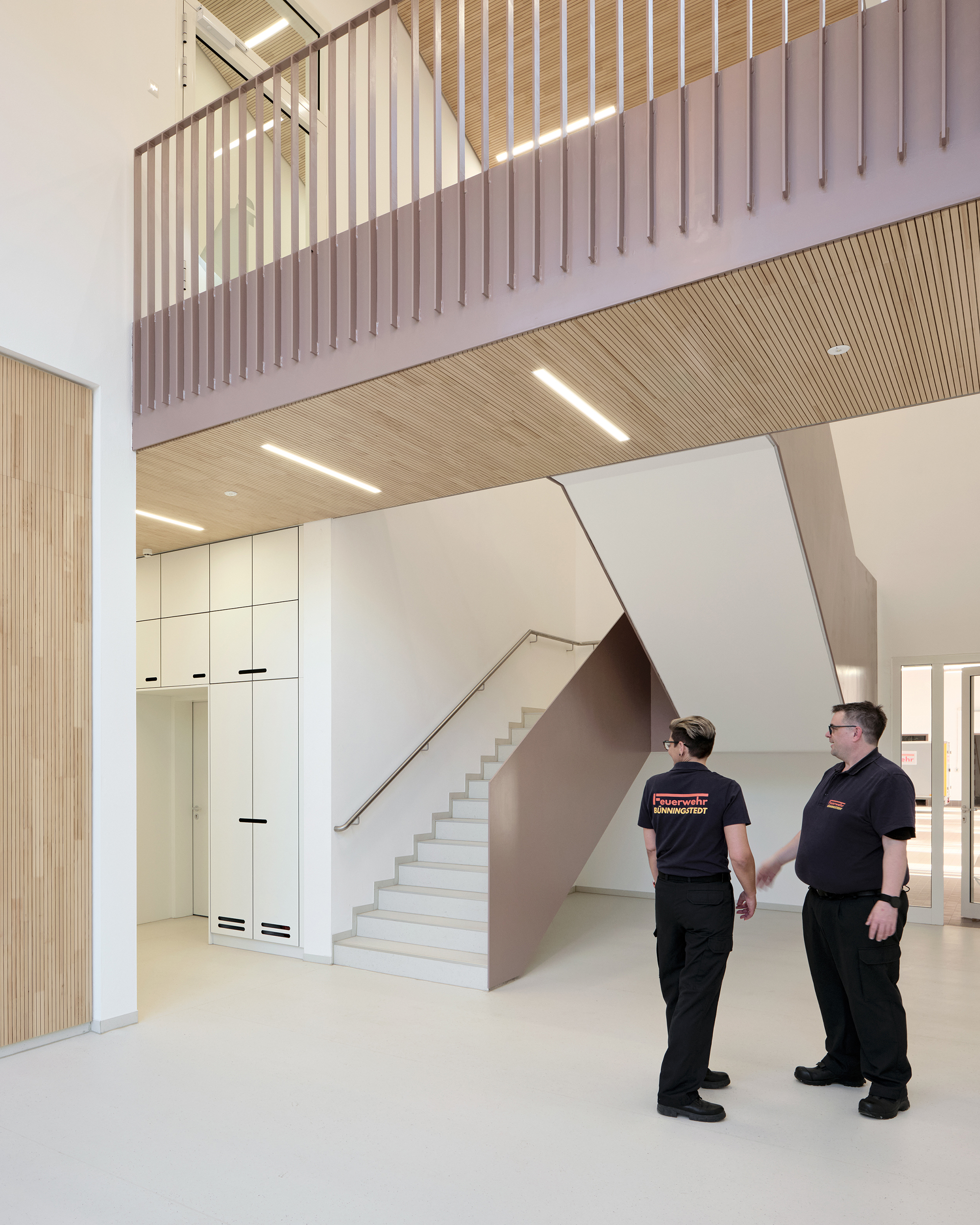 Eine Außenaufnahme eines Feuerwehrhauses mit geöffneten Toren zur Fahrzeughalle, in der vier Einsatzfahrzeuge stehen. Die Fassade ist aus rotbraunem Metall.