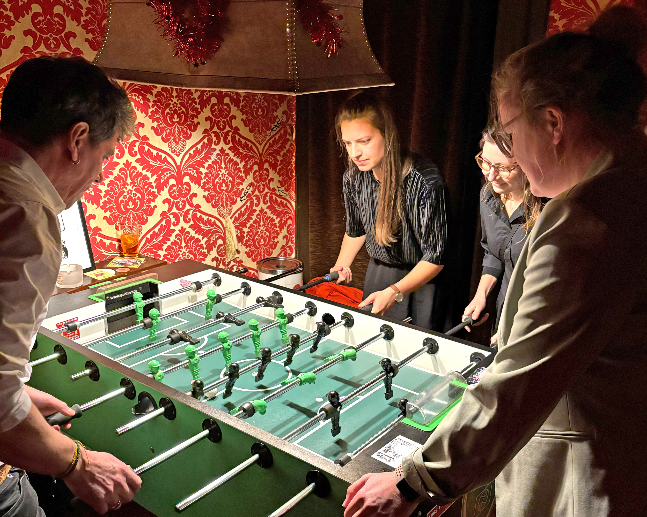 Vier Personen spielen Tischkicker in einem Raum mit warmer Atmosphäre.