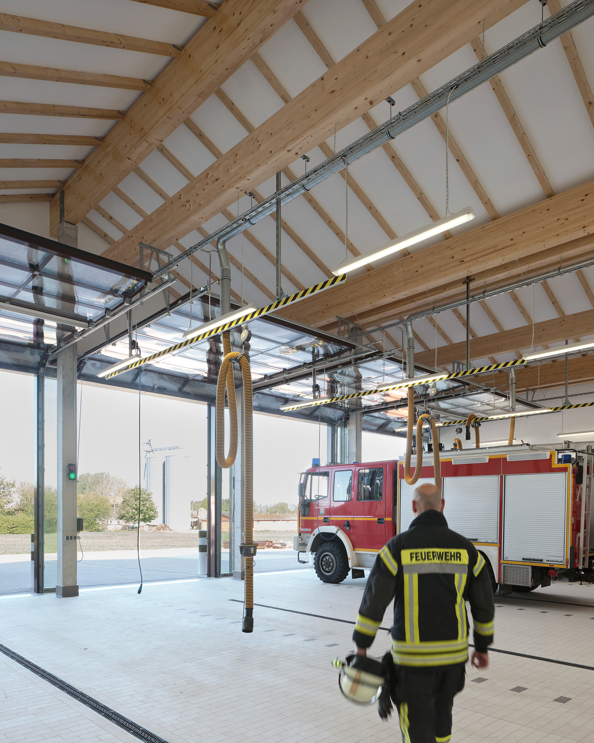 Innenraum einer Fahrzeughalle einer Feuerwache mit zwei Einsatz-Fahrzeugen und einem Feuerwehrmann