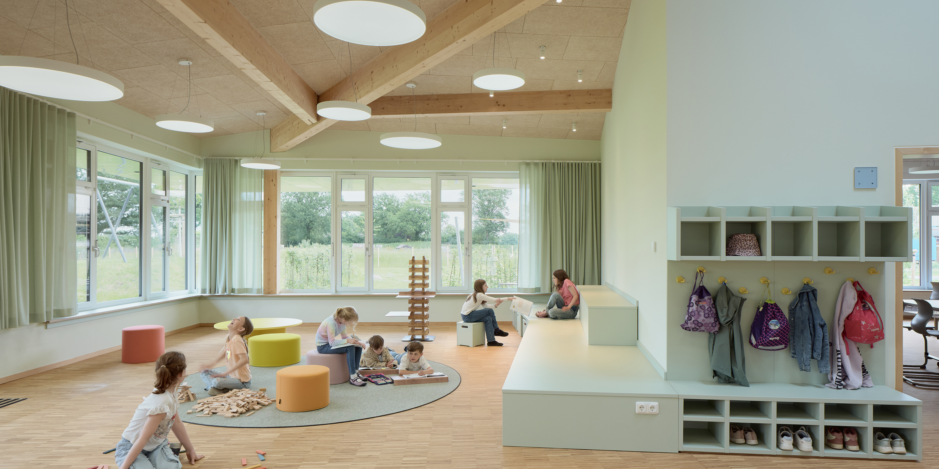 Kinder sitzen, spielen und lernen auf einem Teppich mit mit Möbeln in einem Vorbereich eines Klassenzimmers