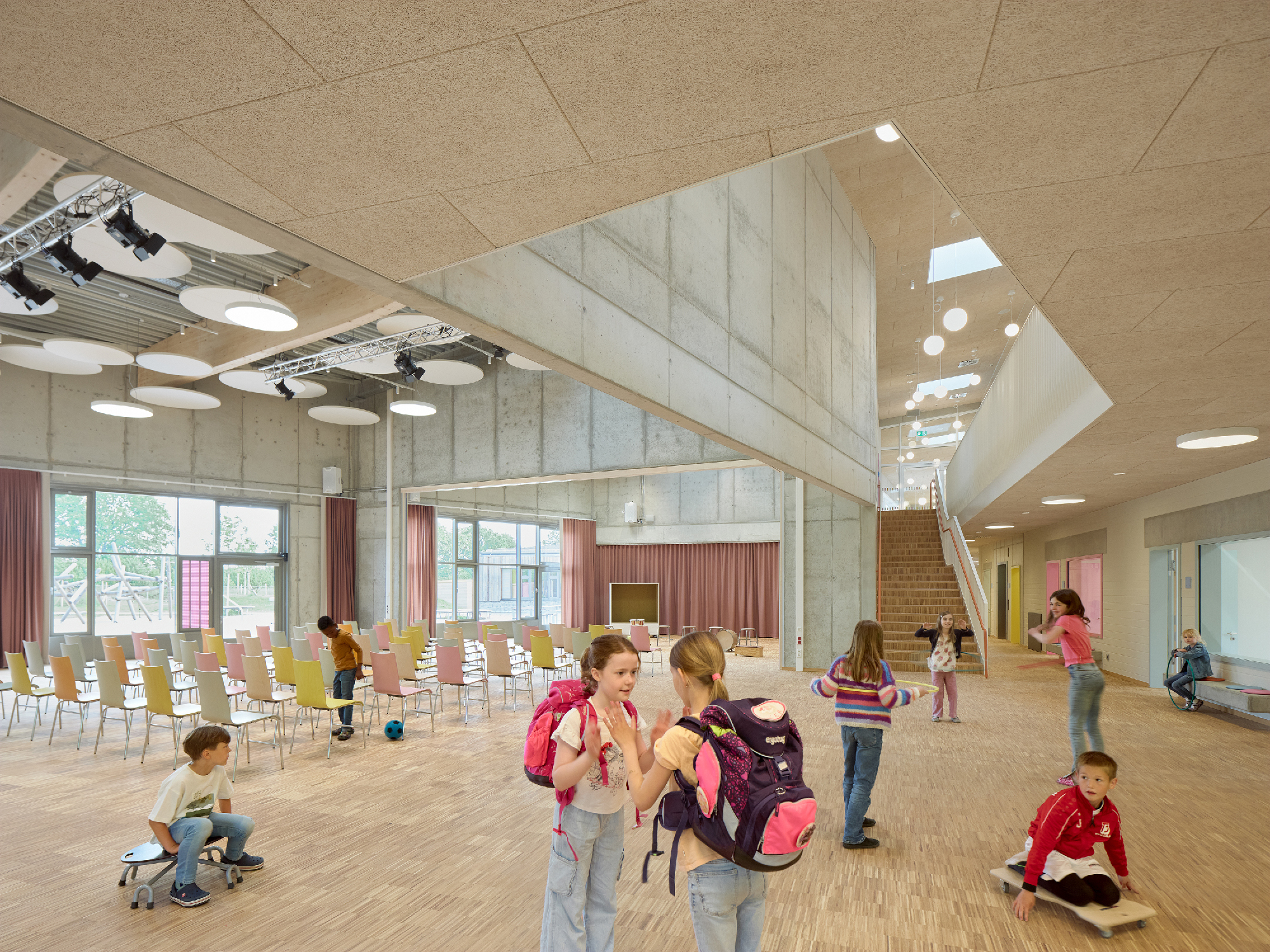 Kinder im Foyer einer Schule mit Treppe und Sitzmöglichkeiten