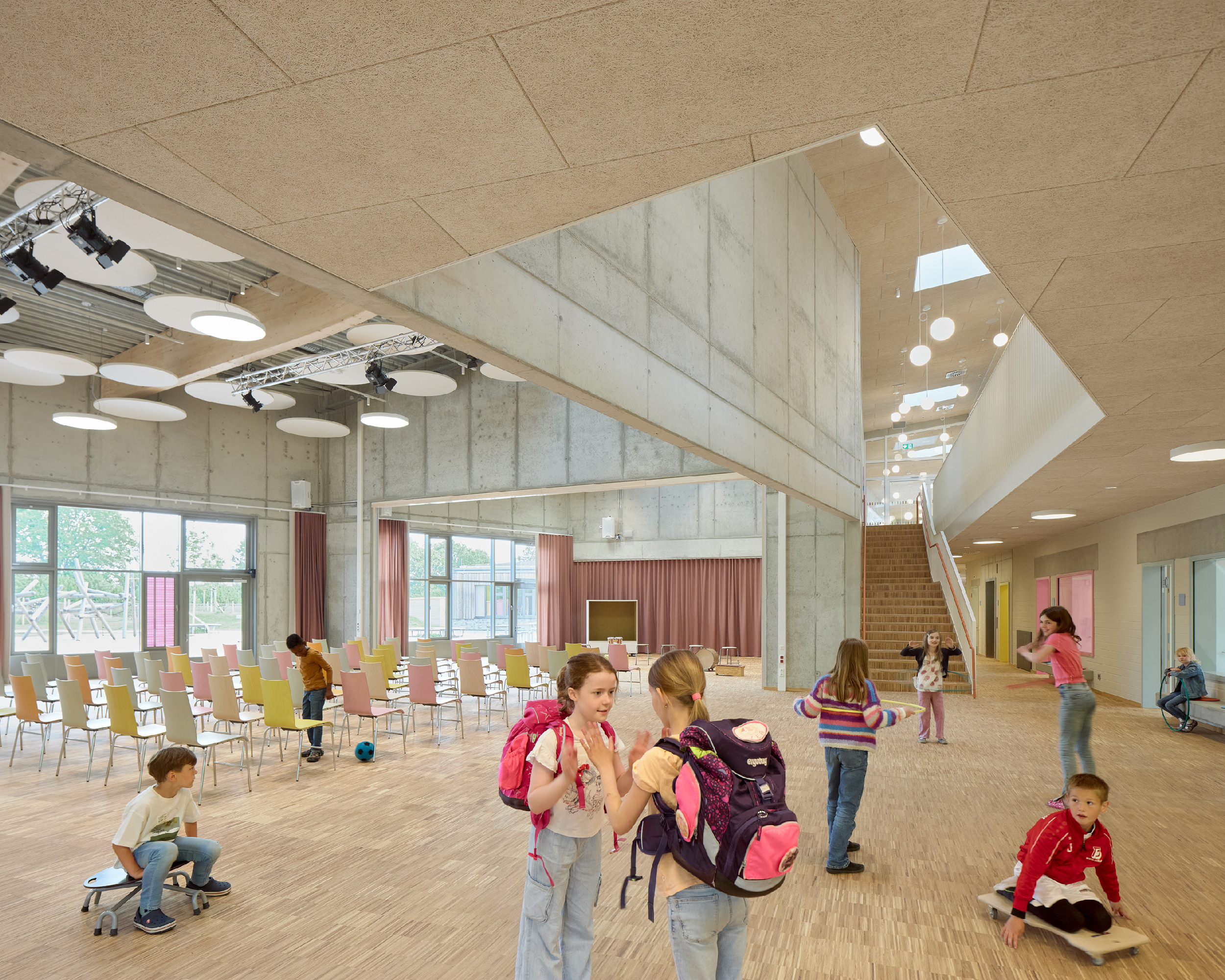 Kinder im Foyer einer Schule mit Treppe und Sitzmöglichkeiten