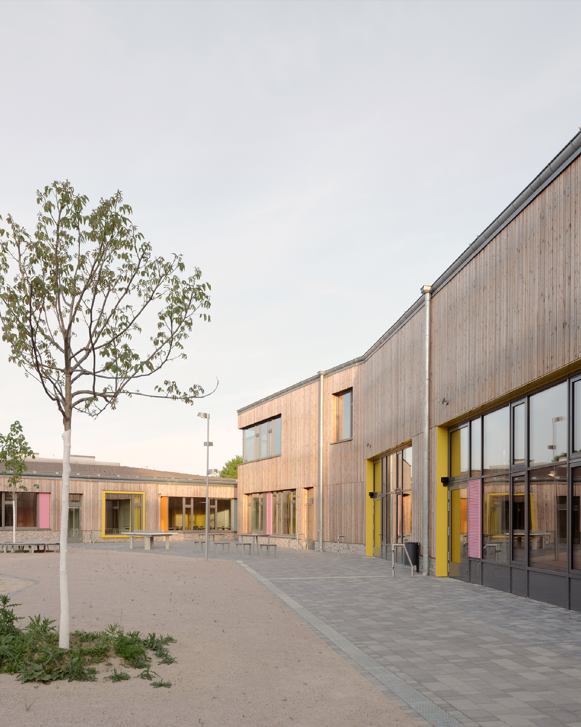 Außenaufnahme eines Schulgebäudes mit Holzfassade und und großen Fenstern. Kräftige Farben betonen Fenster und Eingangsbereich.