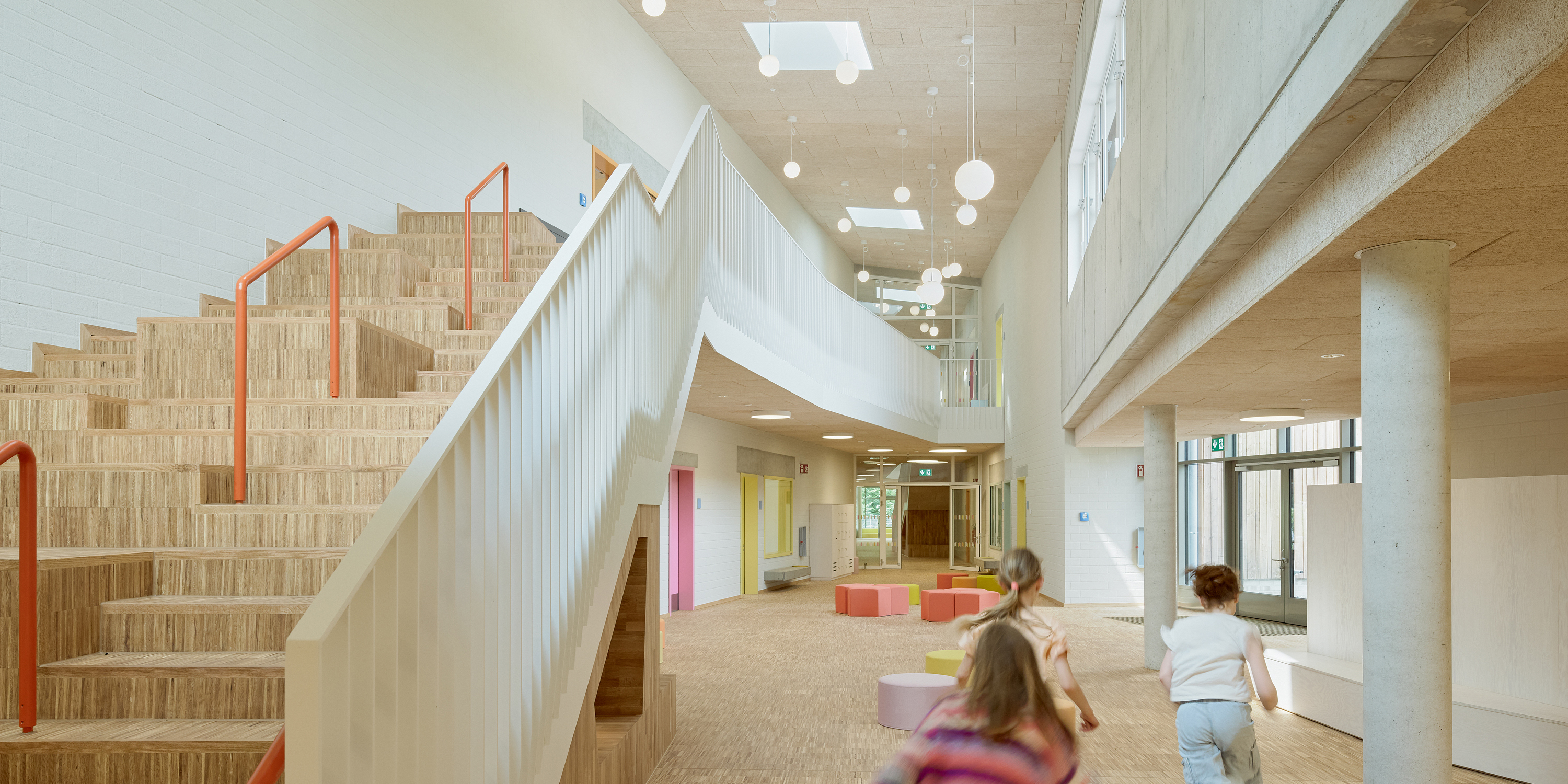 Innenraum einer Schule mit Treppe, Garderobenmöbel und Sitzmöglichkeiten und rennenden Kindern