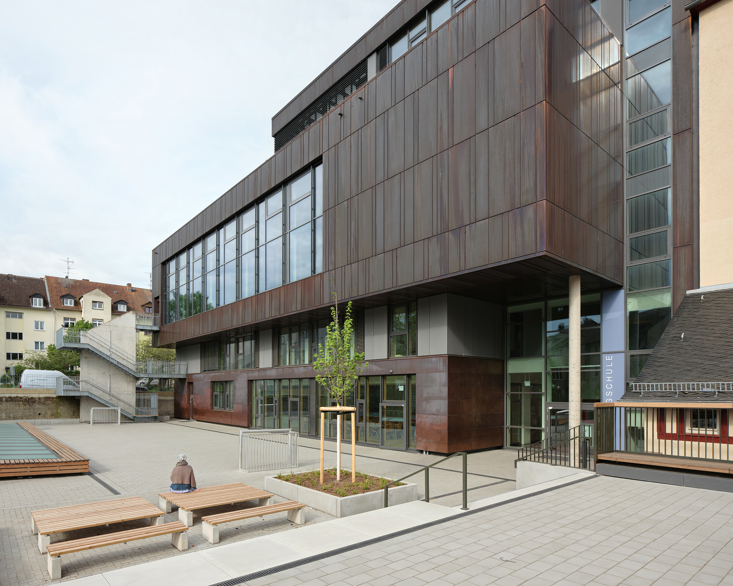 Ein Schulneubau mit dunkler Metallfassade und Schulhof mit Außenmobiliar