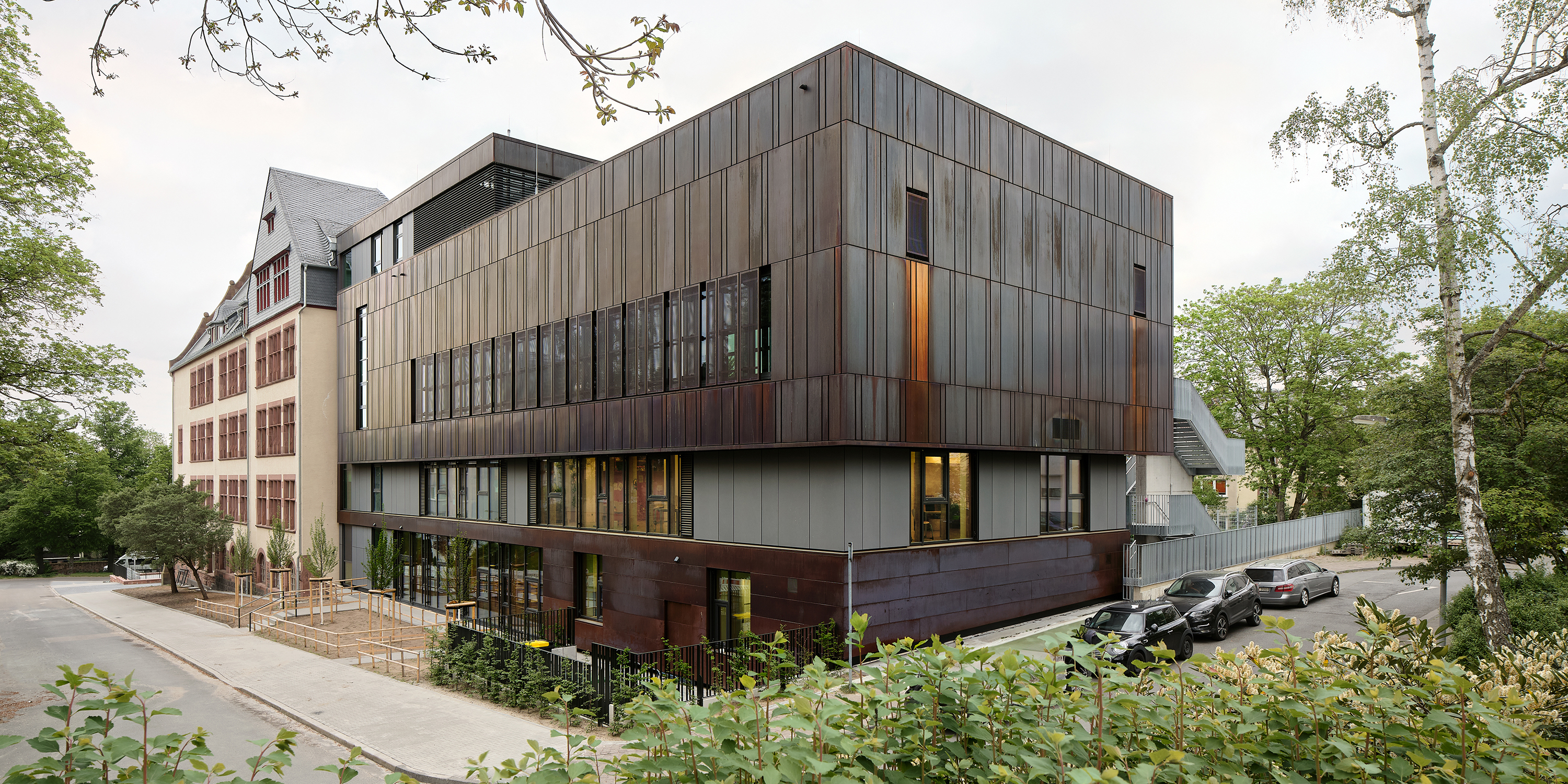 Moderner Anbau mit dunkler Metallfassade verlängert den Altbau mit Sandsteinfassade
