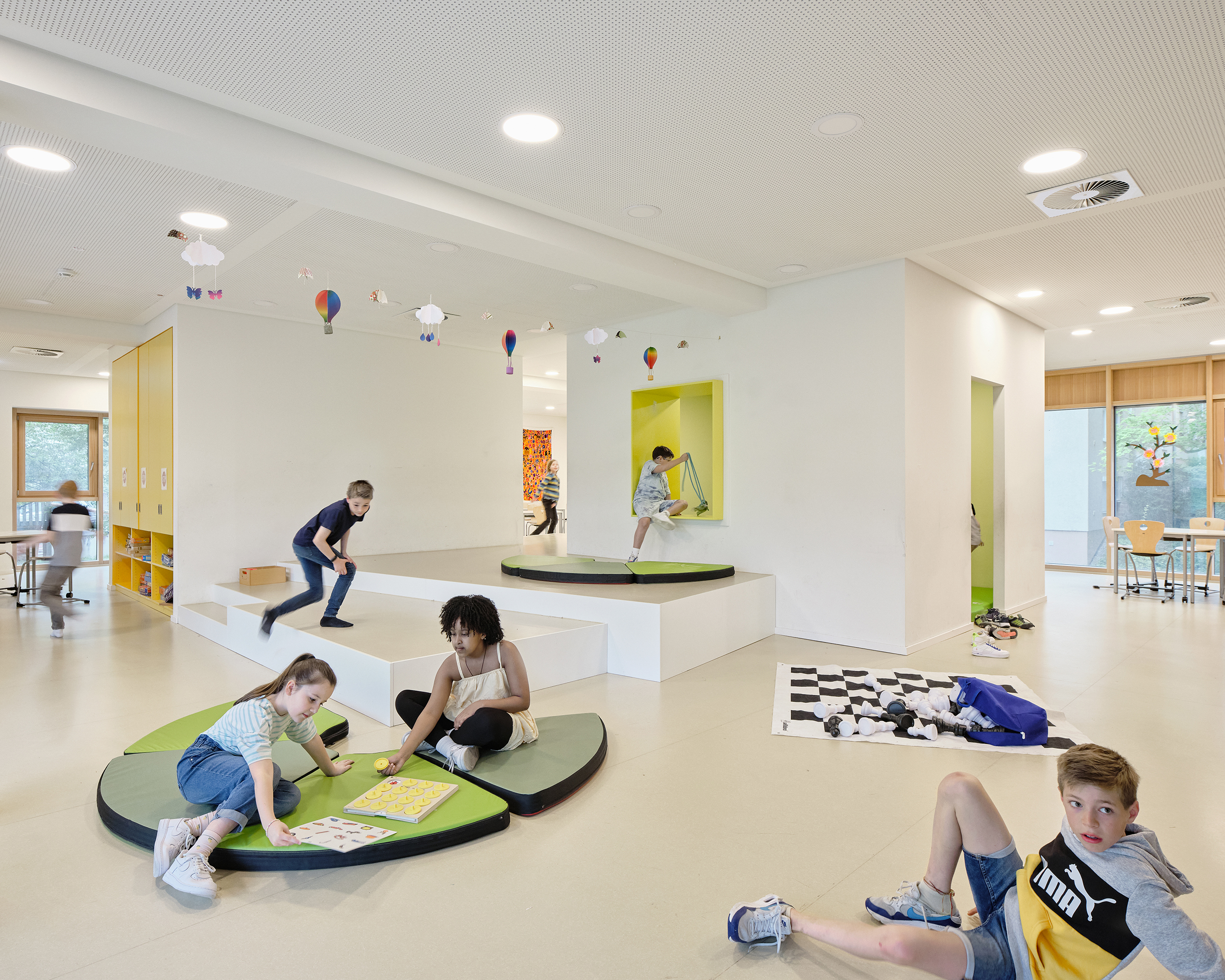 Kinder spielen im Ganztagesbereich einer Schule auf Podesten, Matten und Höhlen