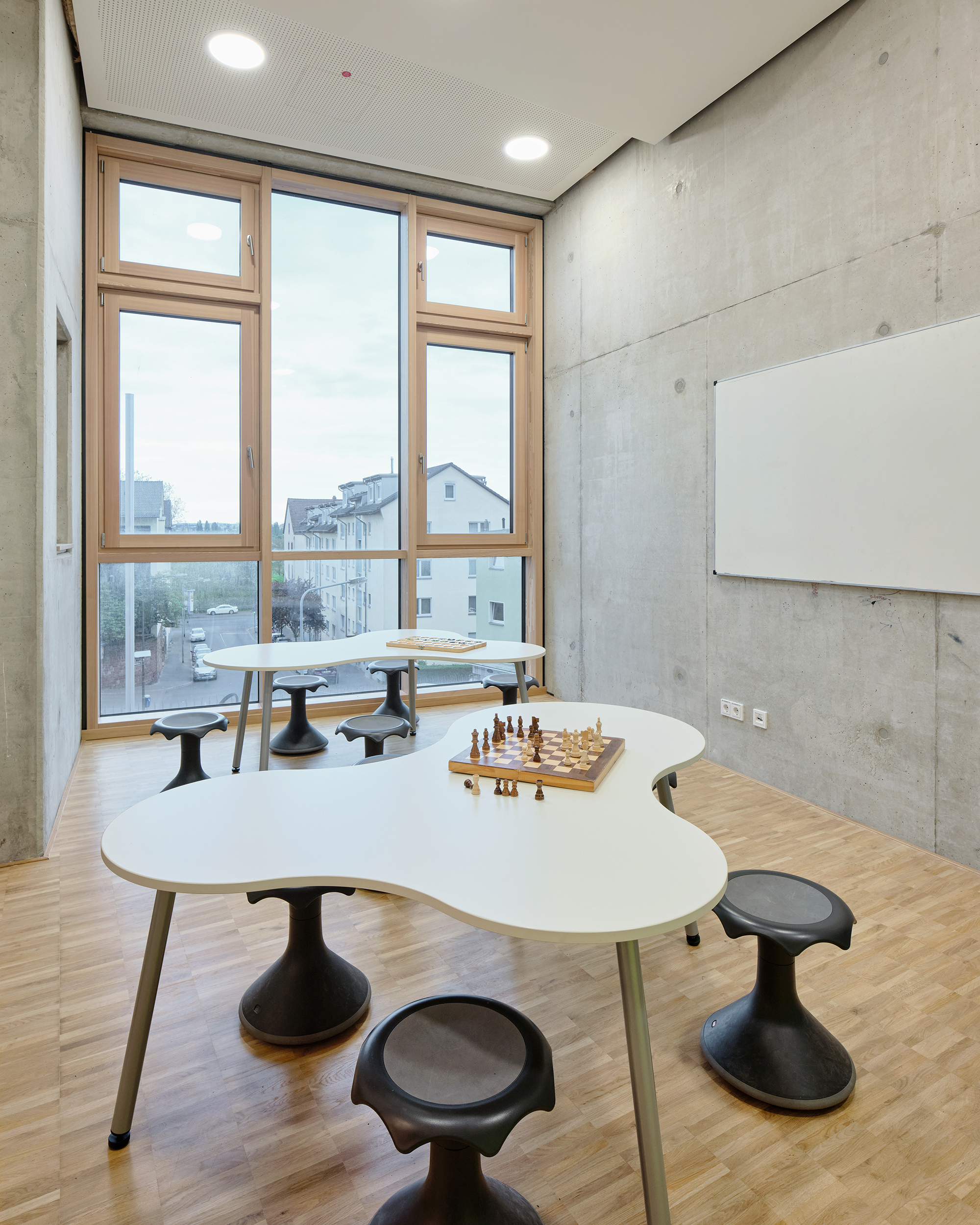Ein Innenraum einer Schule mit blumenartigen Tischen und Hockern und Ausblick auf die Stadt