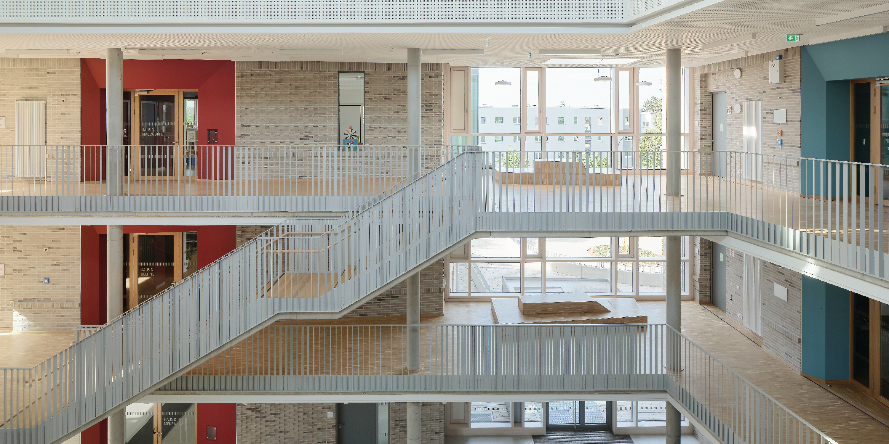 Das Atrium einer Schule mit umlaufenden Galerien, Treppen und großem Oberlicht.