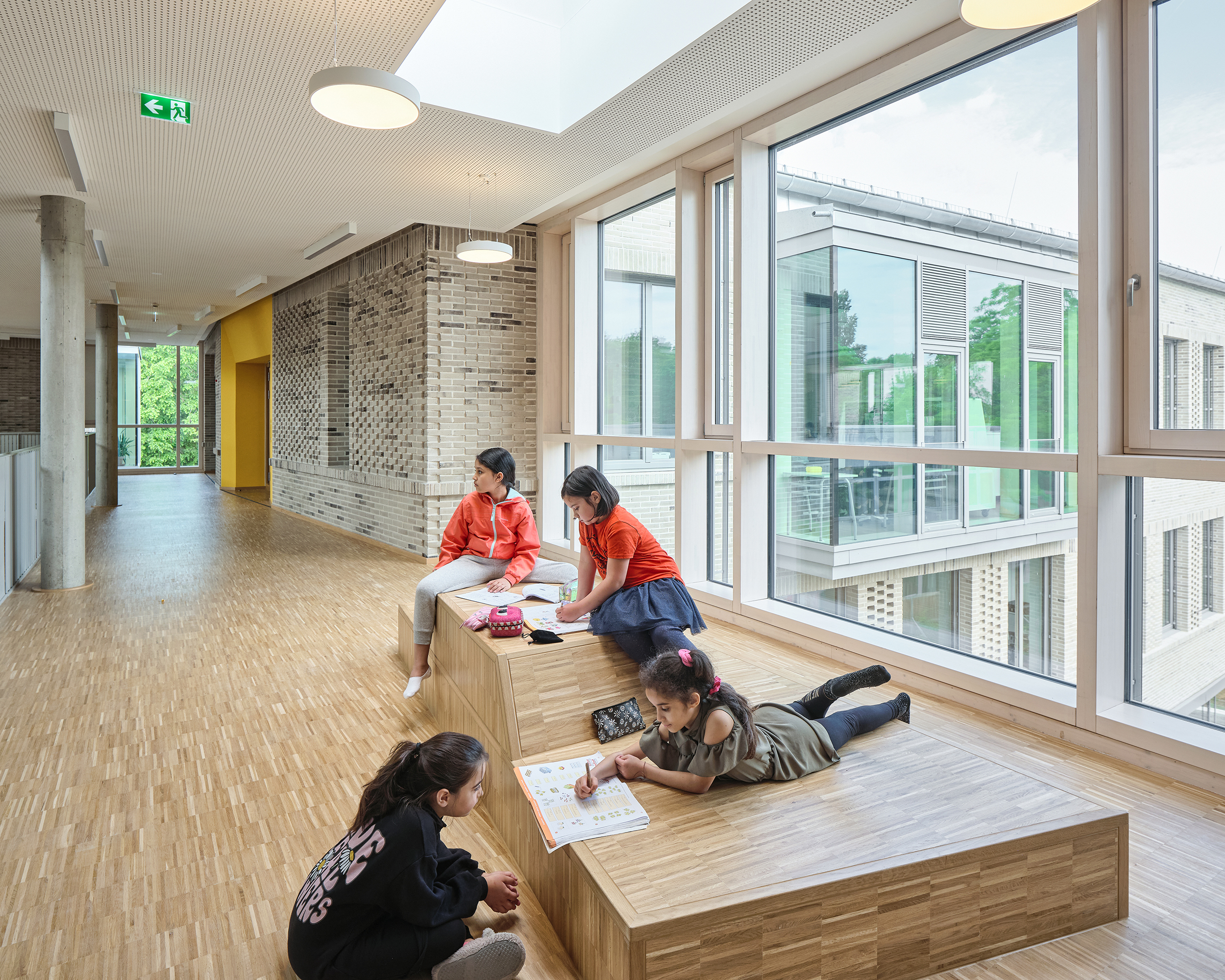 Kinder lernen auf einem mehrfach gefalteten Posest. Das Einbaumöbel aus Holz befindet sich auf der Galerie einer Schule.