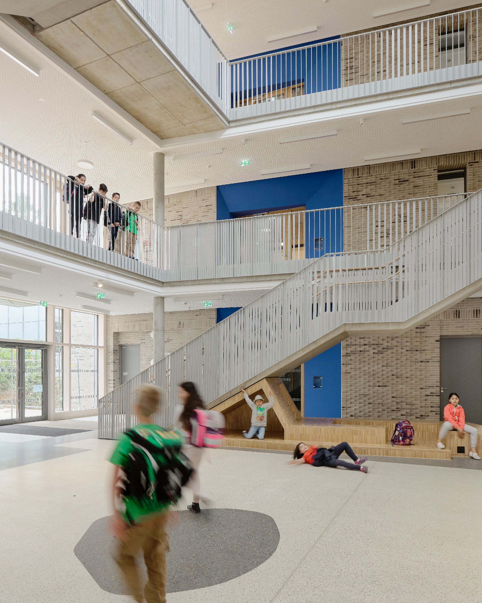 Kinder bewegen sich im Atrium in einer Schule mit Treppen in unterschiedlichen Richtungen, Galerien und einem Einbaumöbel.