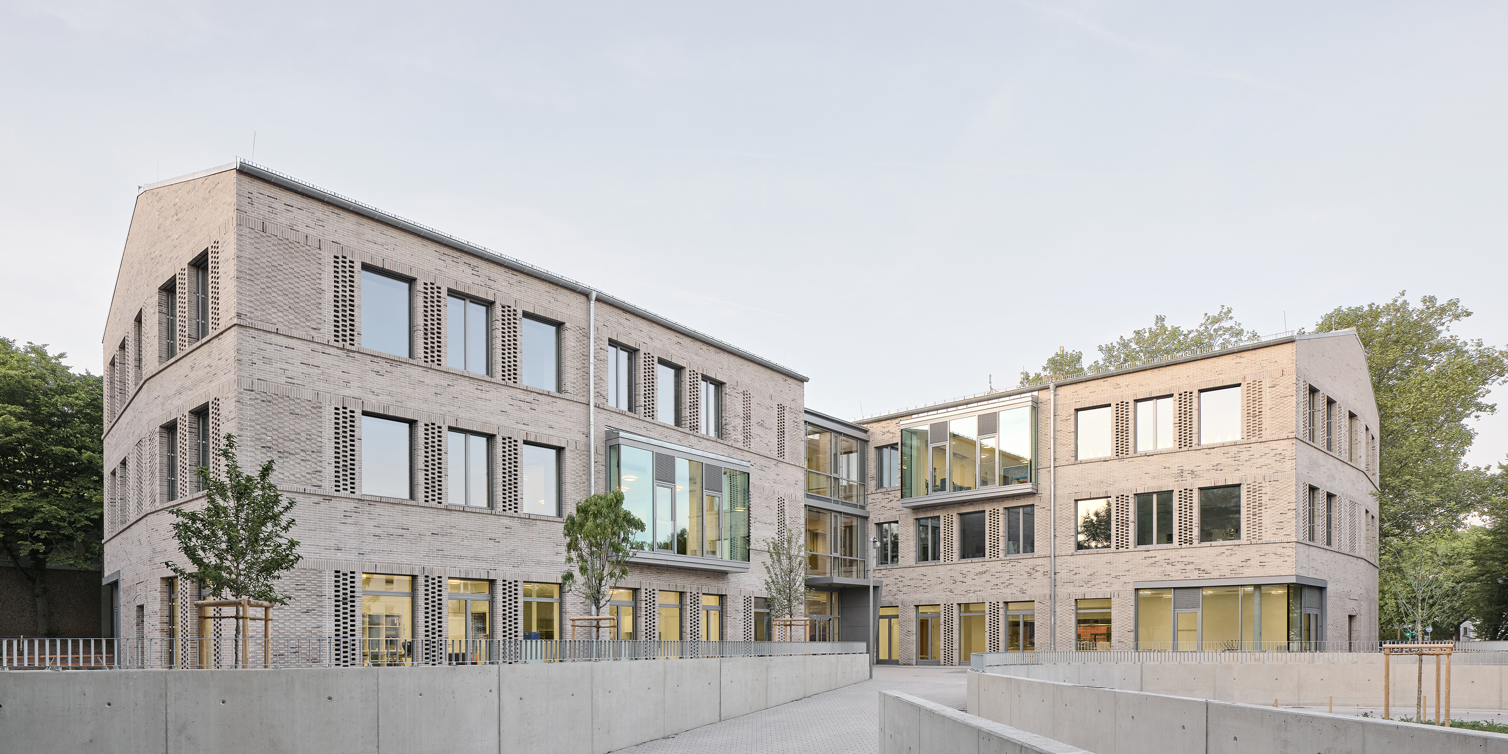 Zwei Flügel eines Schulgebäudes mit heller klinkerfassade und großen Fenstern